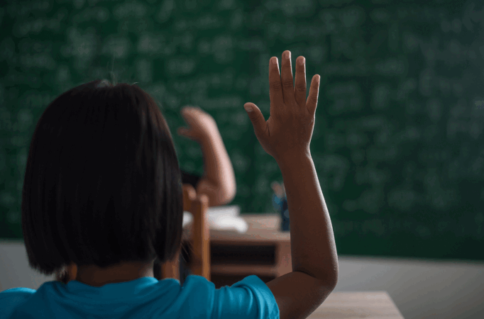 Jovem negra com a mão levantada em sala de aula