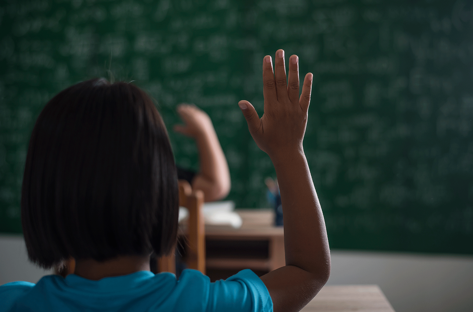 Jovem negra com a mão levantada em sala de aula